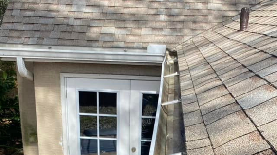 Roof shingles around a dormer with a white-framed window and ladder access beside the chimney.