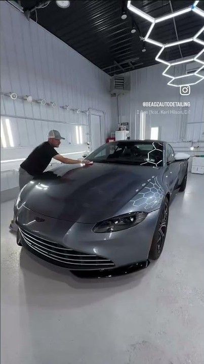 Grey sports car being polished by a person in a bright detailing studio with hexagon ceiling lights