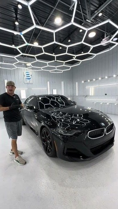 Man standing beside a glossy black BMW in a bright showroom with hexagonal ceiling lights
