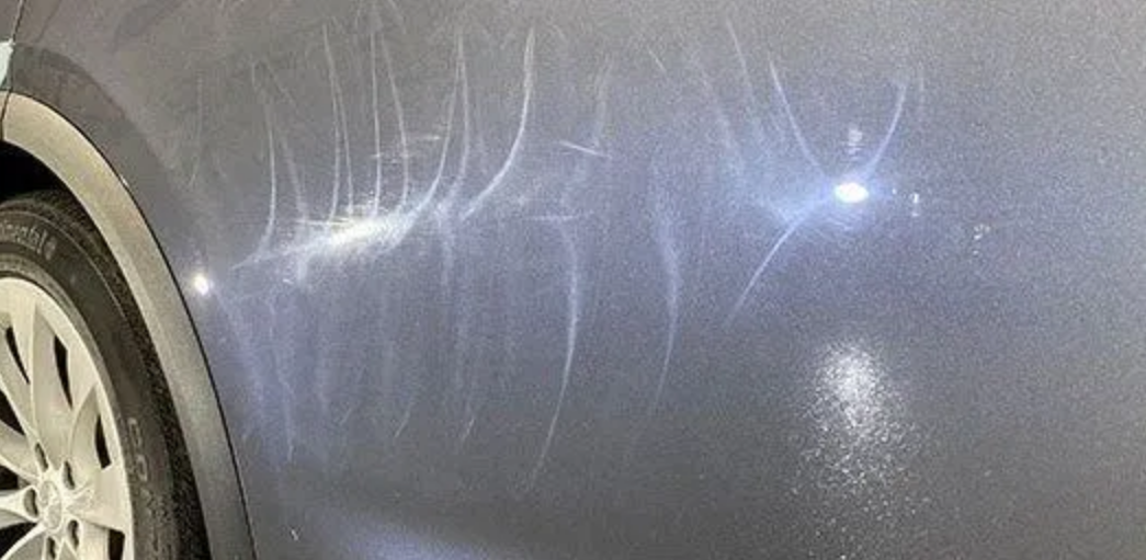 Gray car door with numerous scratches and swirl marks.