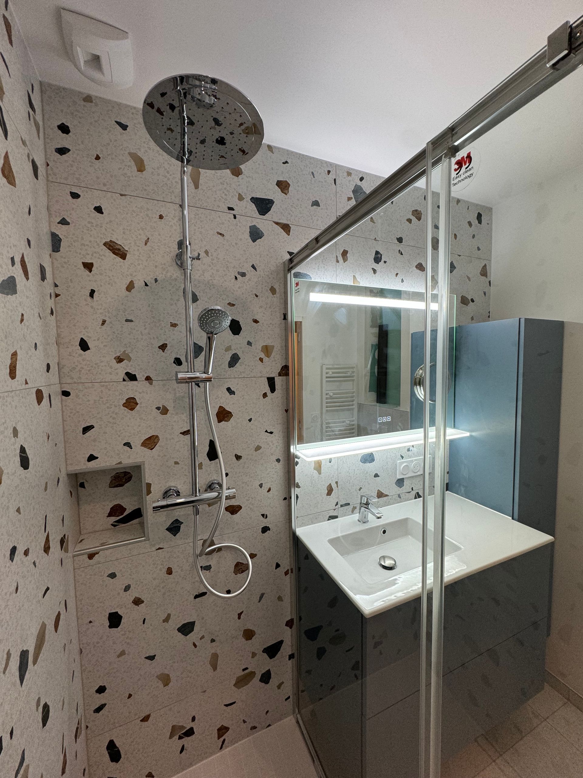 Une salle de bain avec douche, lavabo et miroir