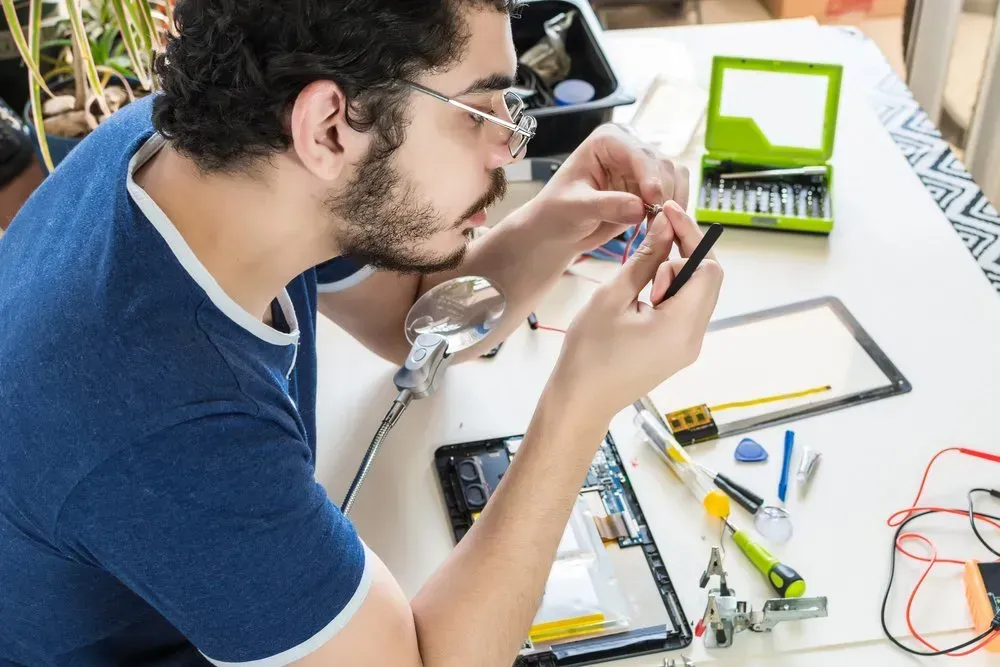 Man with Glasses Repairs a Tablet on A White Table — Rescuetech Computer And iPhone Repairs in Ballina, NSW