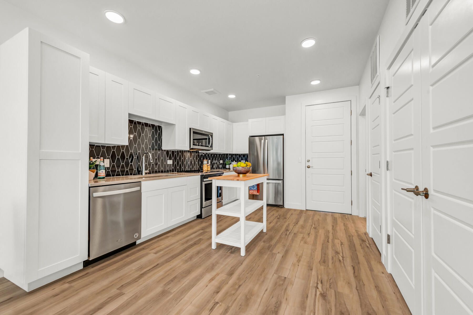 Bright, modern kitchen with white cabinets, stainless steel appliances, and wood-look flooring.
