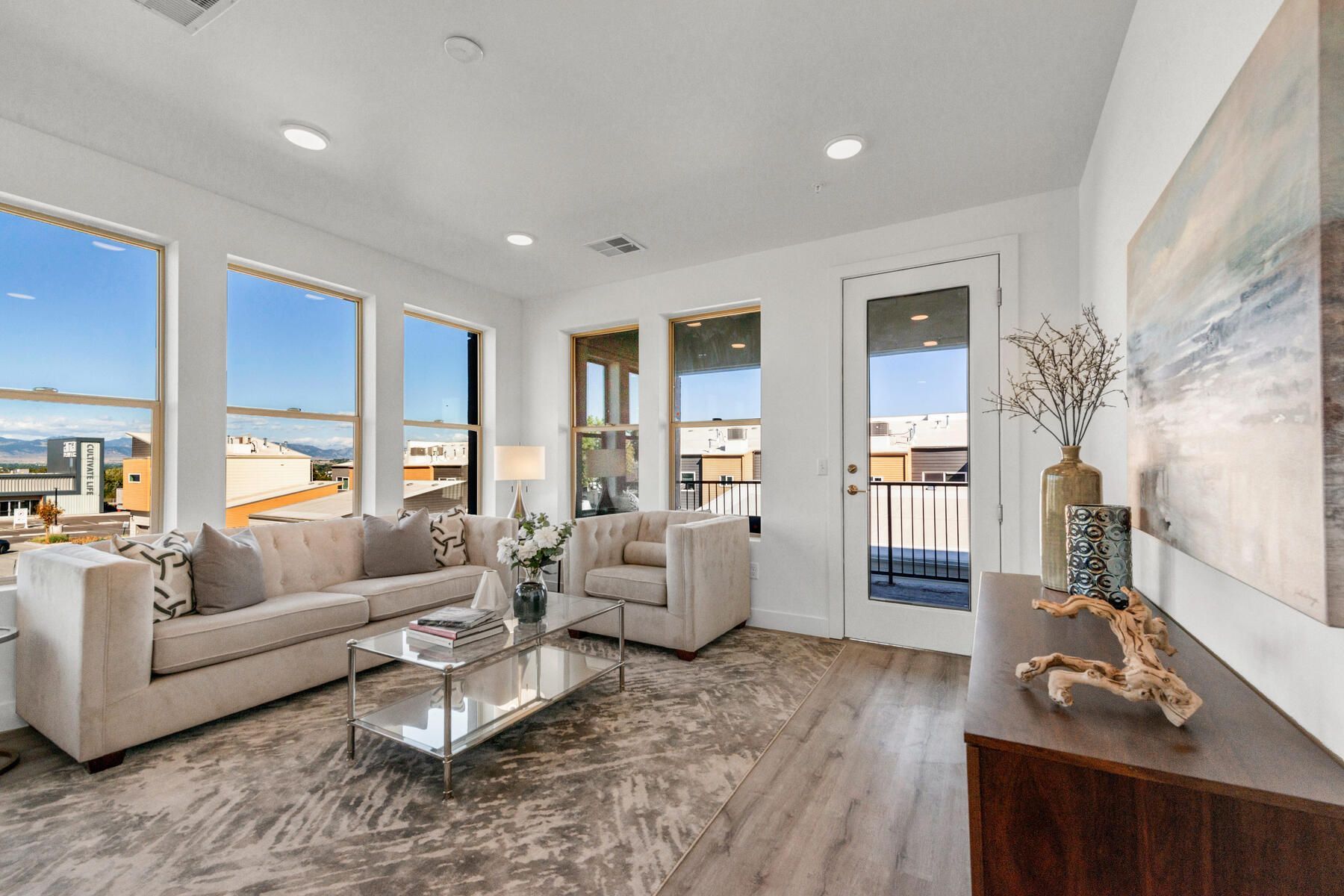 Bright living room with large windows, sofa, chair, coffee table, and door to balcony.