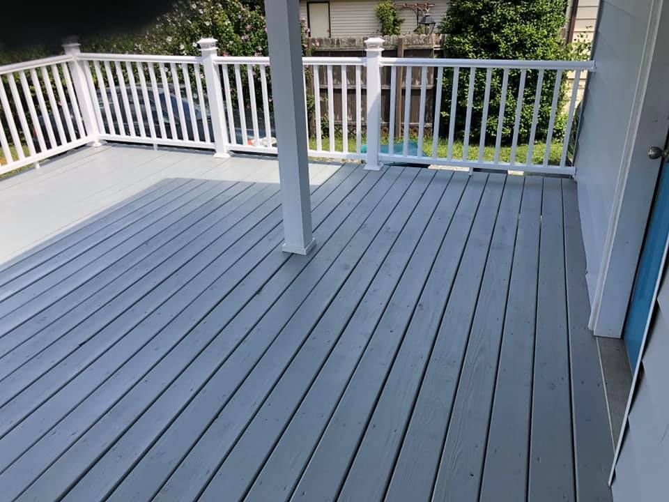 A gray deck with a white railing and a blue door.