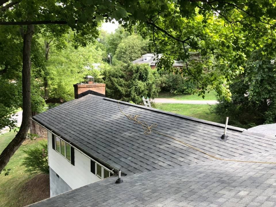 A house with a black roof and a chimney is surrounded by trees.