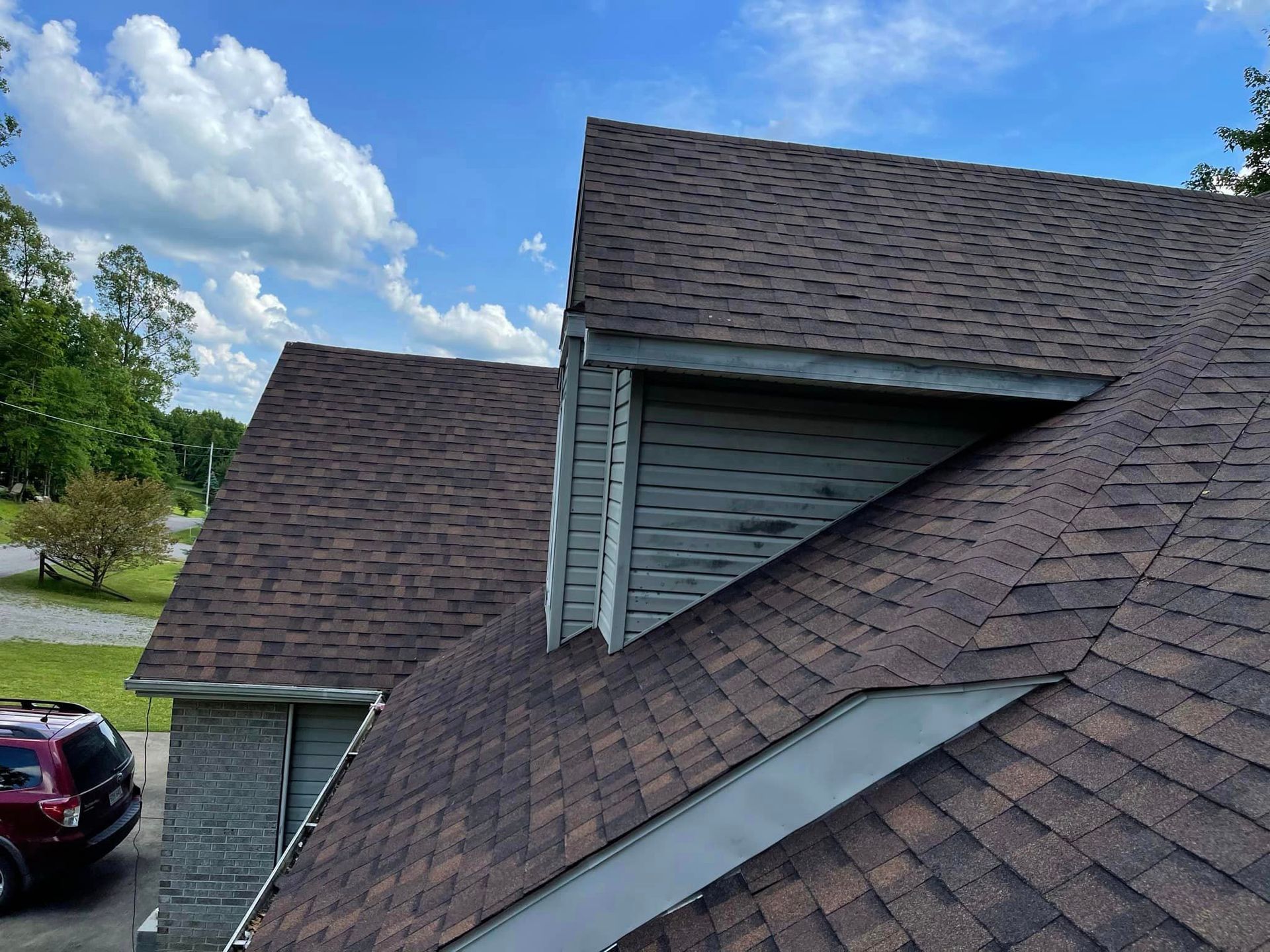 A car is parked in front of a house with a roof that has shingles on it.