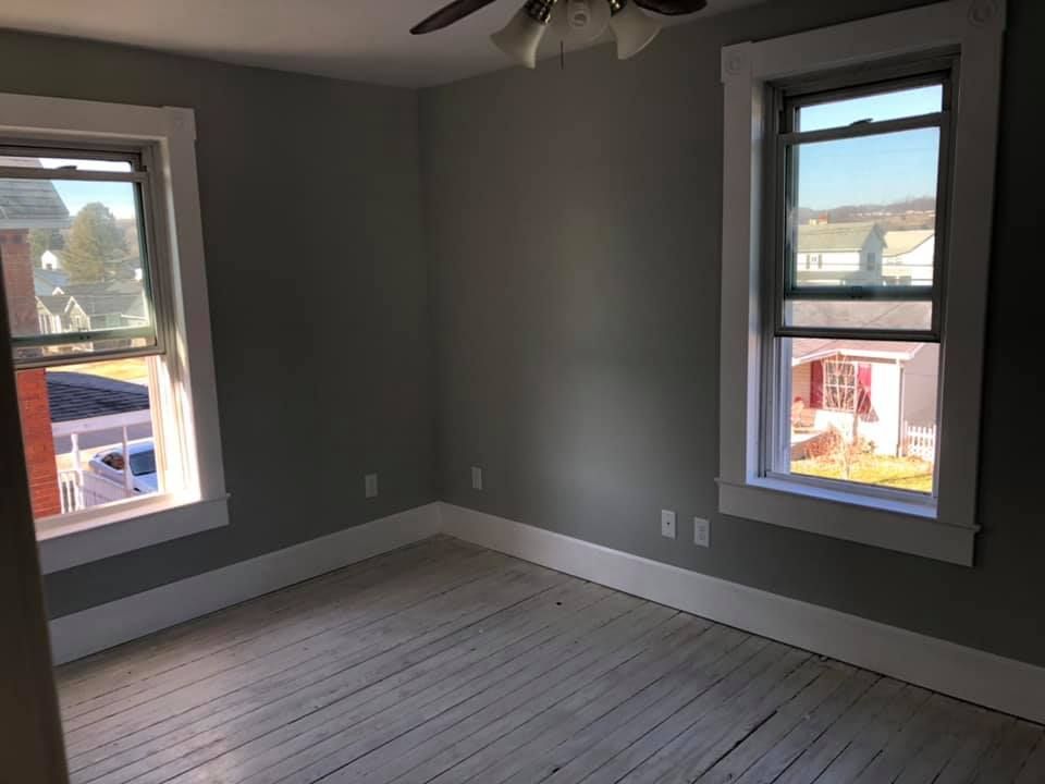 An empty room with two windows and a ceiling fan.