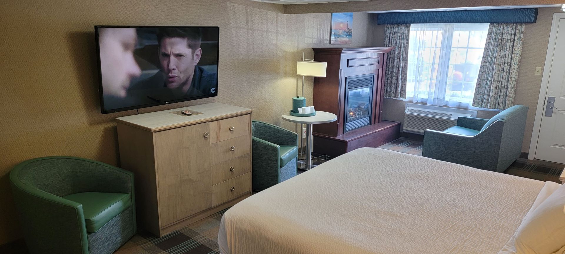 A hotel room with a king size bed , television , chairs and dresser.