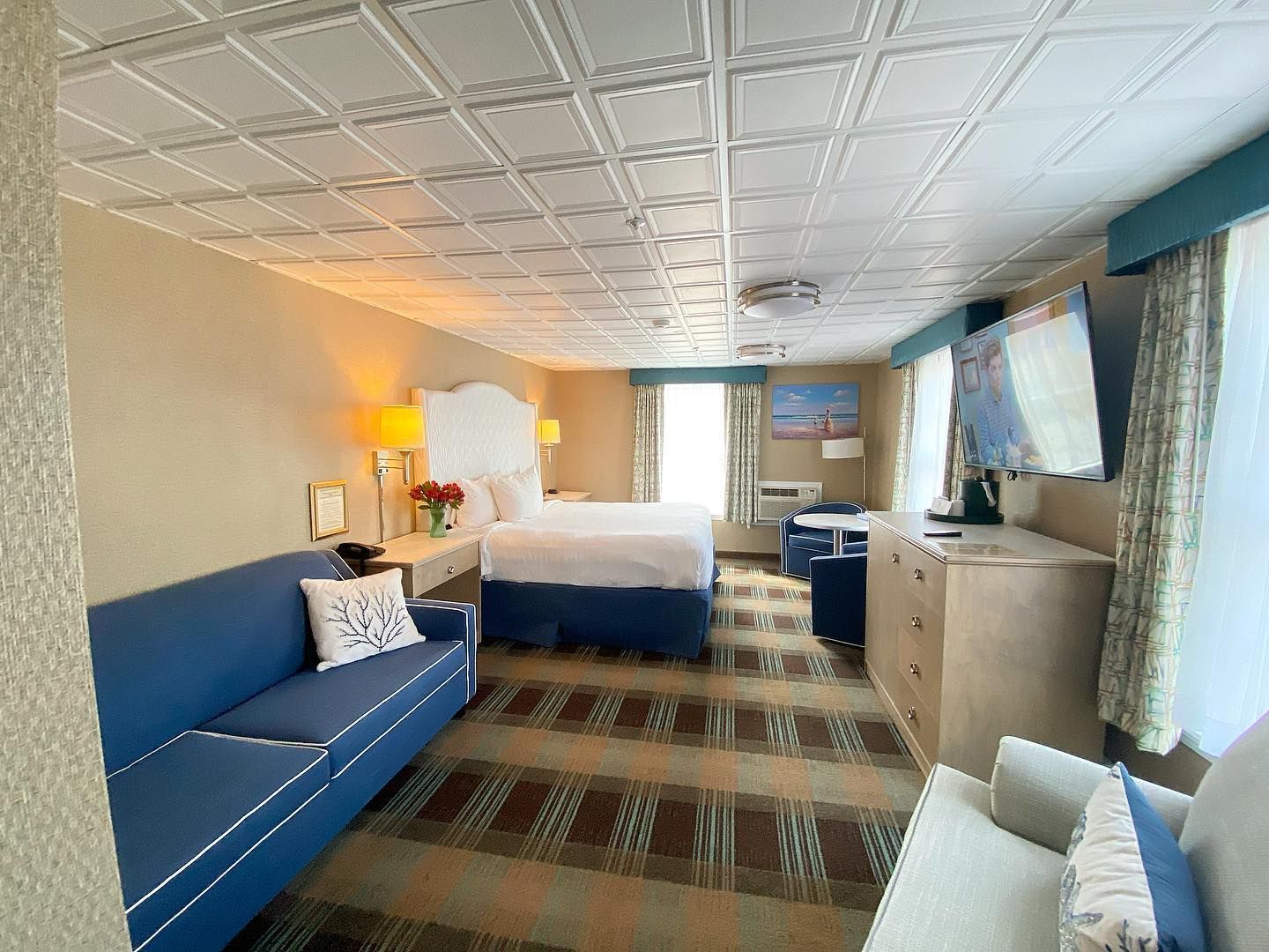 A hotel room with a couch , bed , dresser and television.