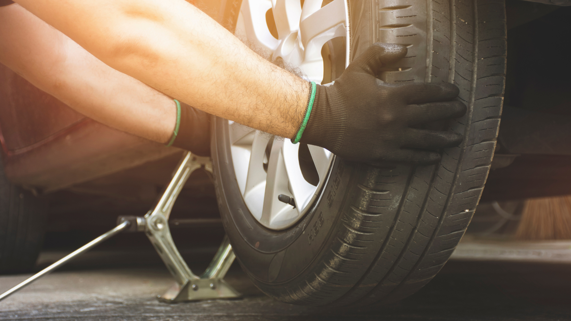 Mechanic’s gloved hand changing a car tire with a jack in a garage