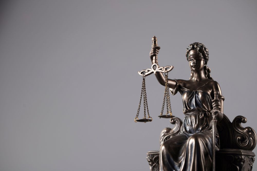 A Statue Of Justice Is Sitting In A Chair Holding Scales Of Justice — McNeilly Lawyers In Kempsey, NSW