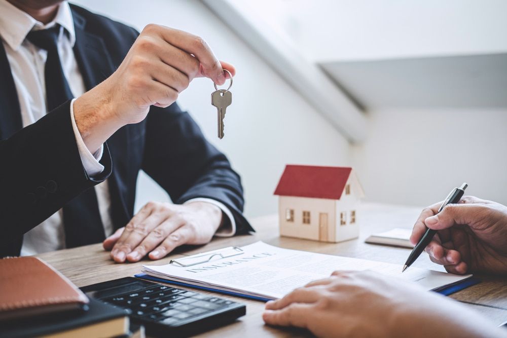 A Man Is Giving A Key To A Woman In Front Of A Model House — McNeilly Lawyers In Kempsey, NSW