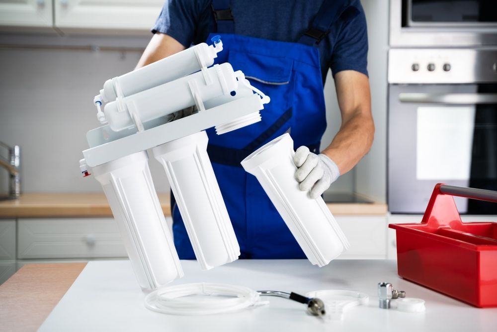 A Man Is Fixing A Water Filter In A Kitchen — Advantage Plumbing Solutions In Boolaroo, NSW