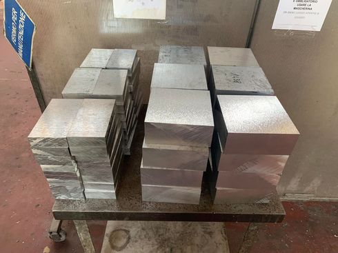 Pile di blocchi di metallo rettangolari su un carrello di metallo, probabilmente in un ambiente di fabbrica.