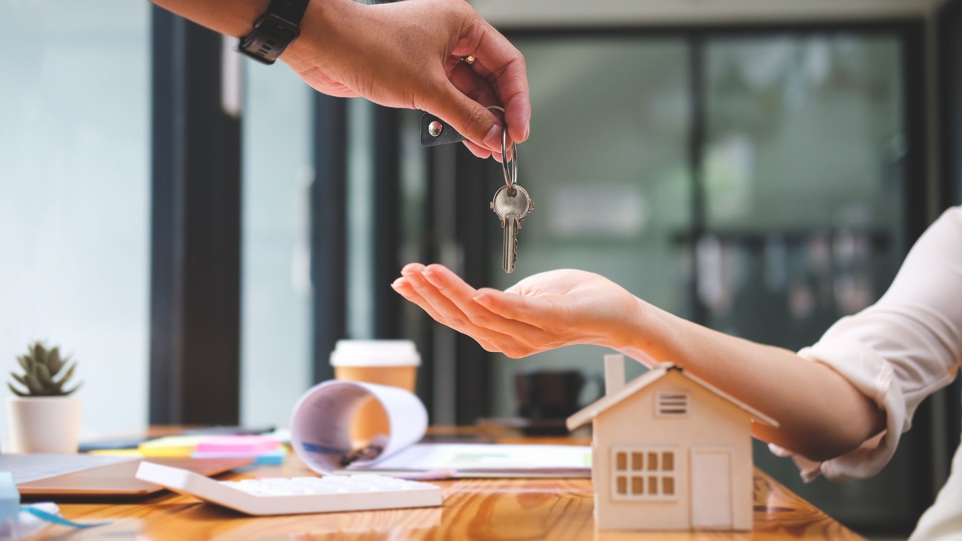 A man is handing a woman a set of keys in front of a model house.