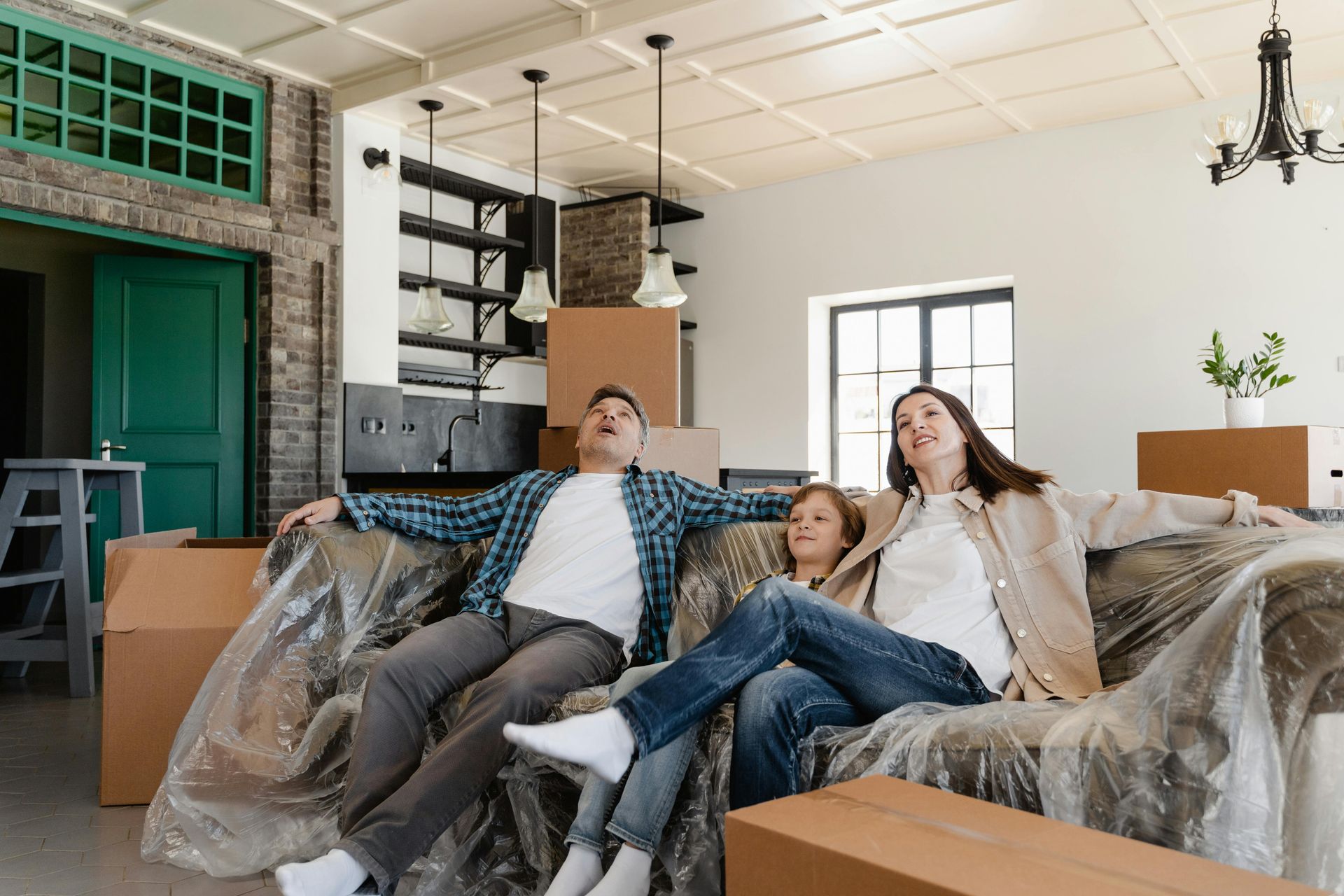 A family is sitting on a couch in a living room covered in plastic.