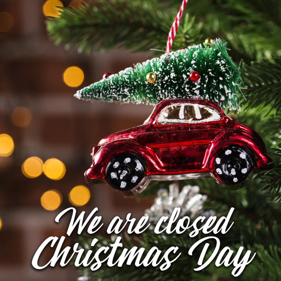 A red vintage car ornament with a Christmas tree on top on a tree, with text reading: We are closed Christmas Day.