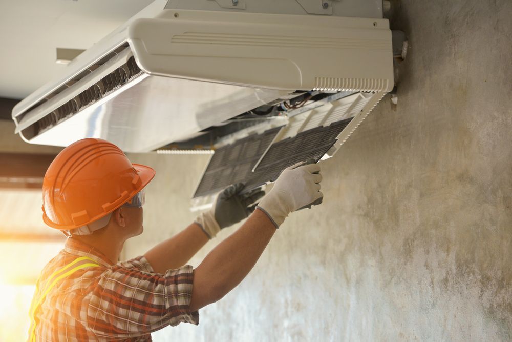 A Man Wearing A Hard Hat And Gloves Is Working On An Air Conditioner — Coastline Air In Tuggerah, NSW