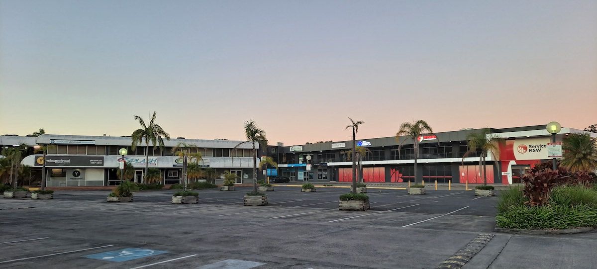 An Empty Parking Lot With Palm Trees In Front Of A Building — Coastline Air In Erina, NSW