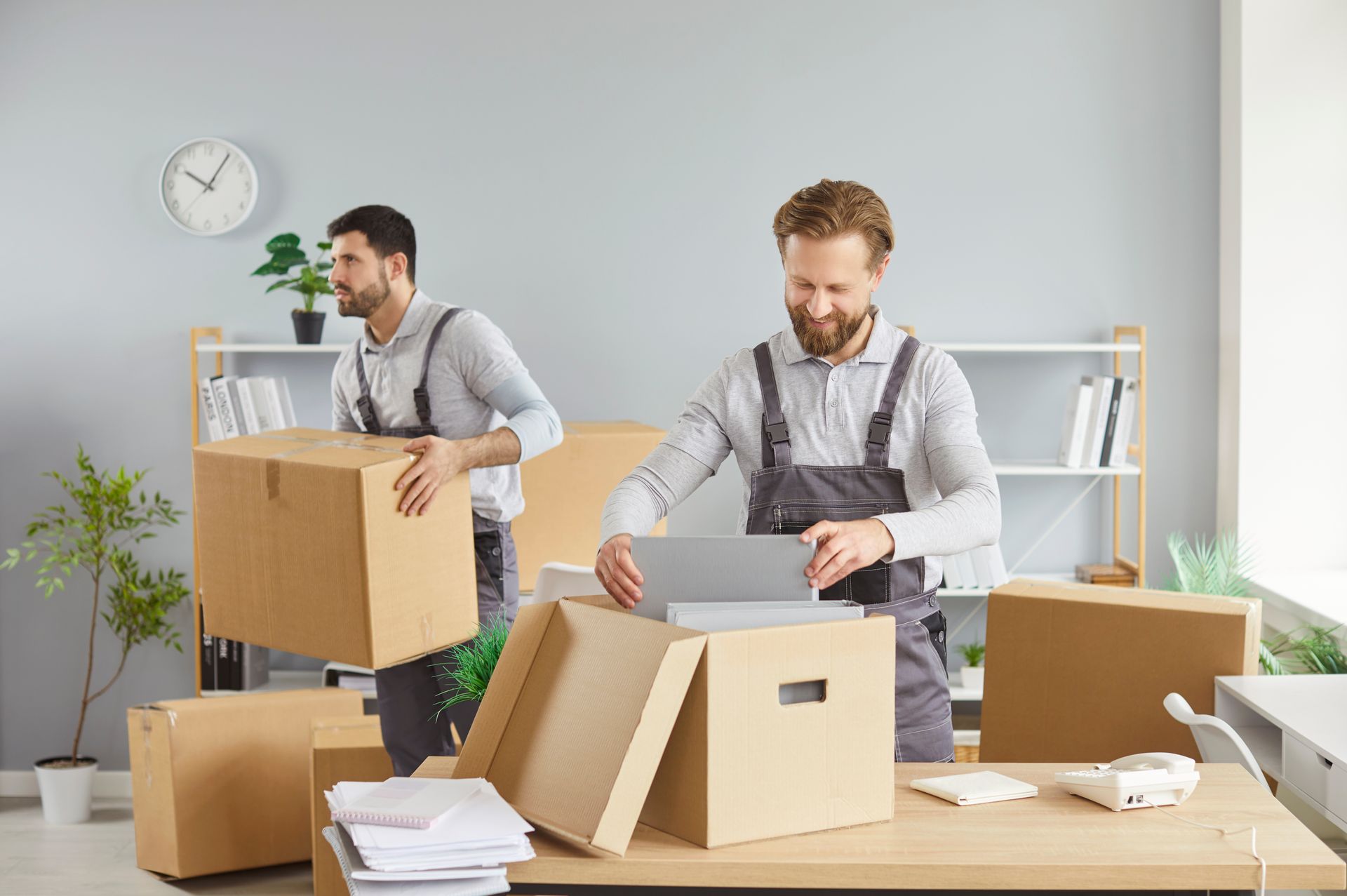 A pair of male movers handle several boxes for a moving, inside an office. A pair of male movers handle several boxes for a moving, inside an office.