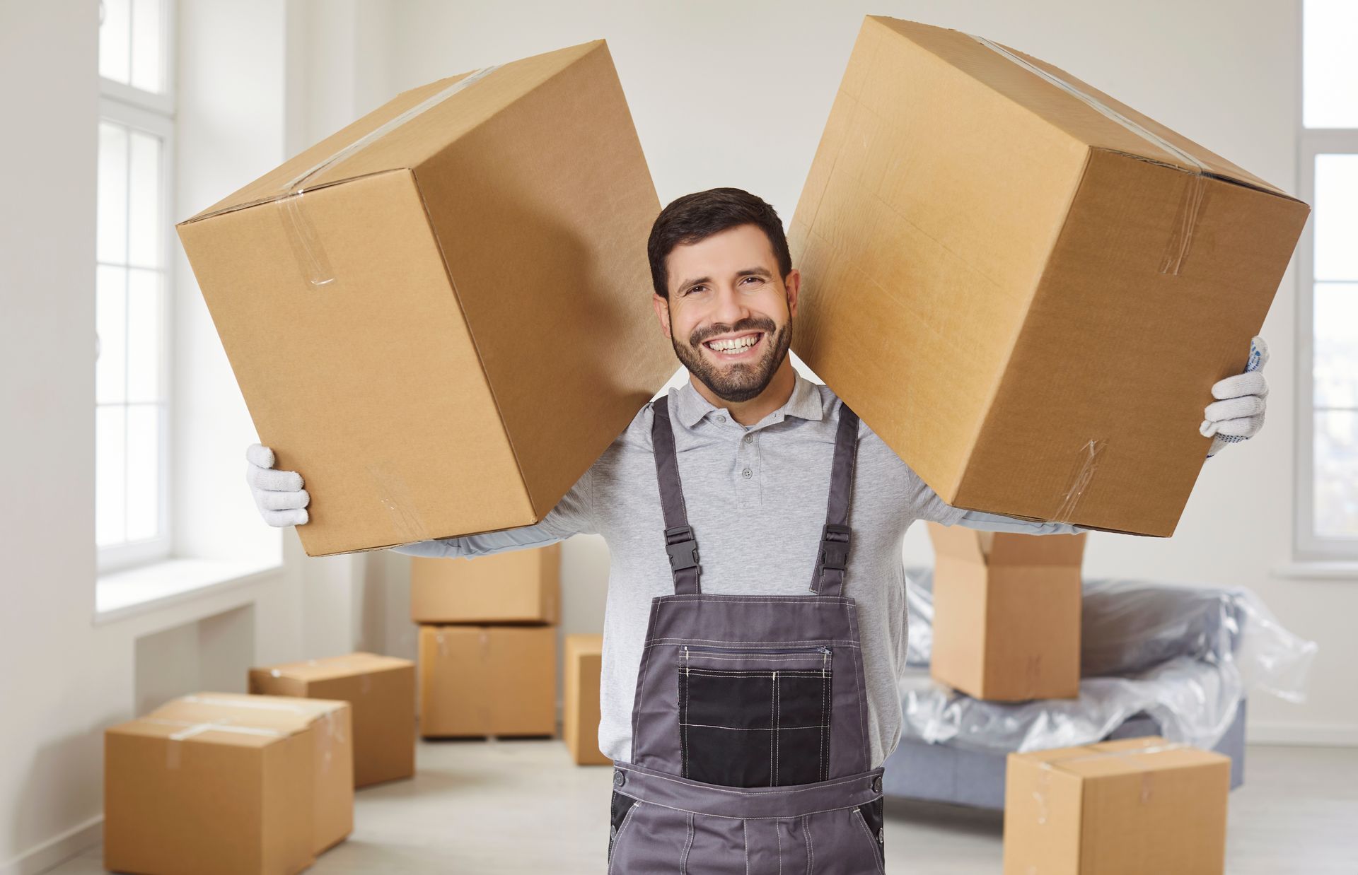 A male mover smiles to the camera while holding boxes. A male mover smiles to the camera while holding boxes.
