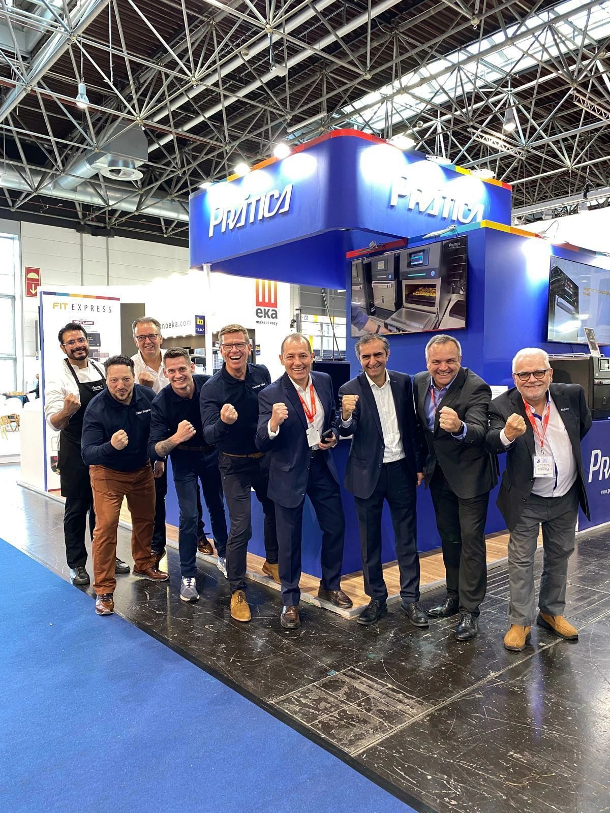Group of men in suits and casual wear at a trade show booth. Blue and white booth with the word