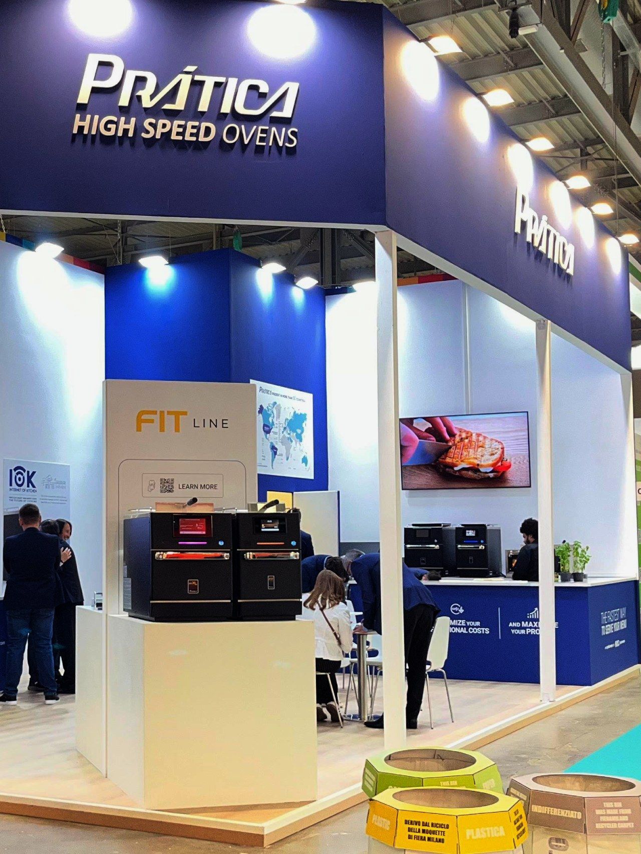 Prática high-speed ovens booth at a trade show; blue, white booth; ovens, digital display; people milling around.
