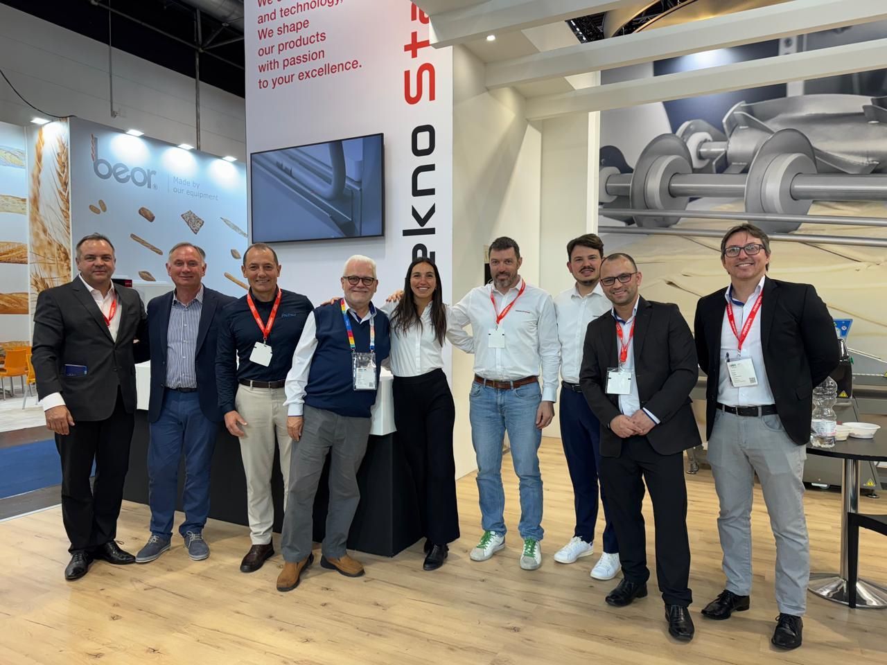 Group of nine people posing in front of a trade show booth.