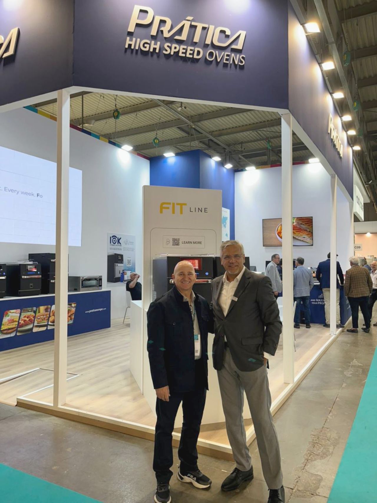 Two men pose in front of a booth at a trade show with 