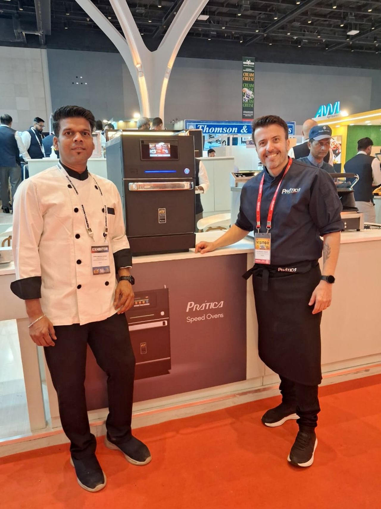Two chefs posing next to a black oven with a product display at a trade show.