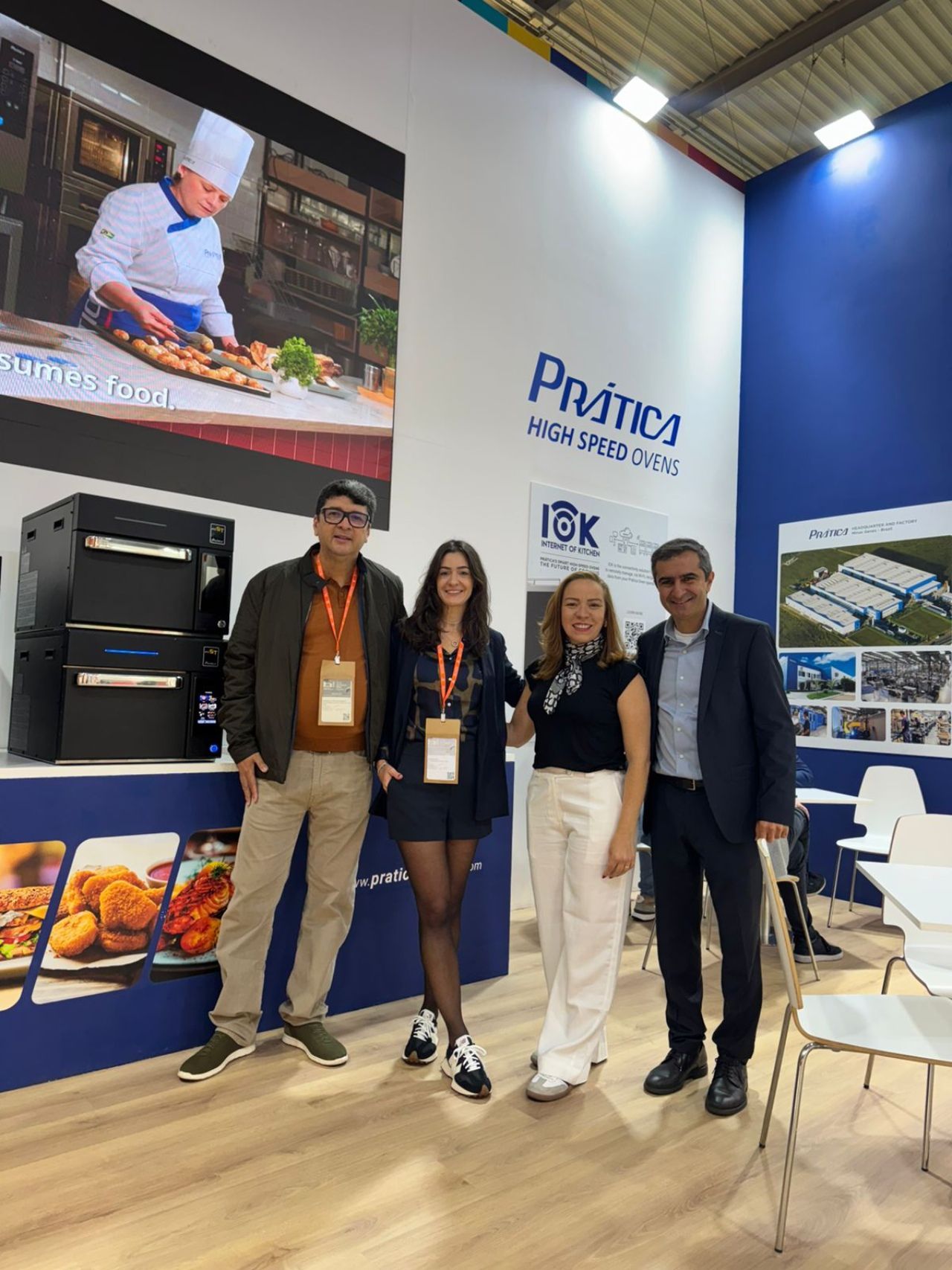 Four people pose at a trade show booth with cooking equipment and a logo.
