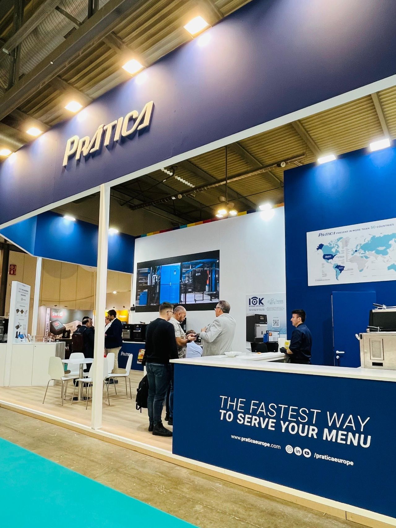 PRATICA booth at a trade show with people interacting. Blue and white colors dominate. 