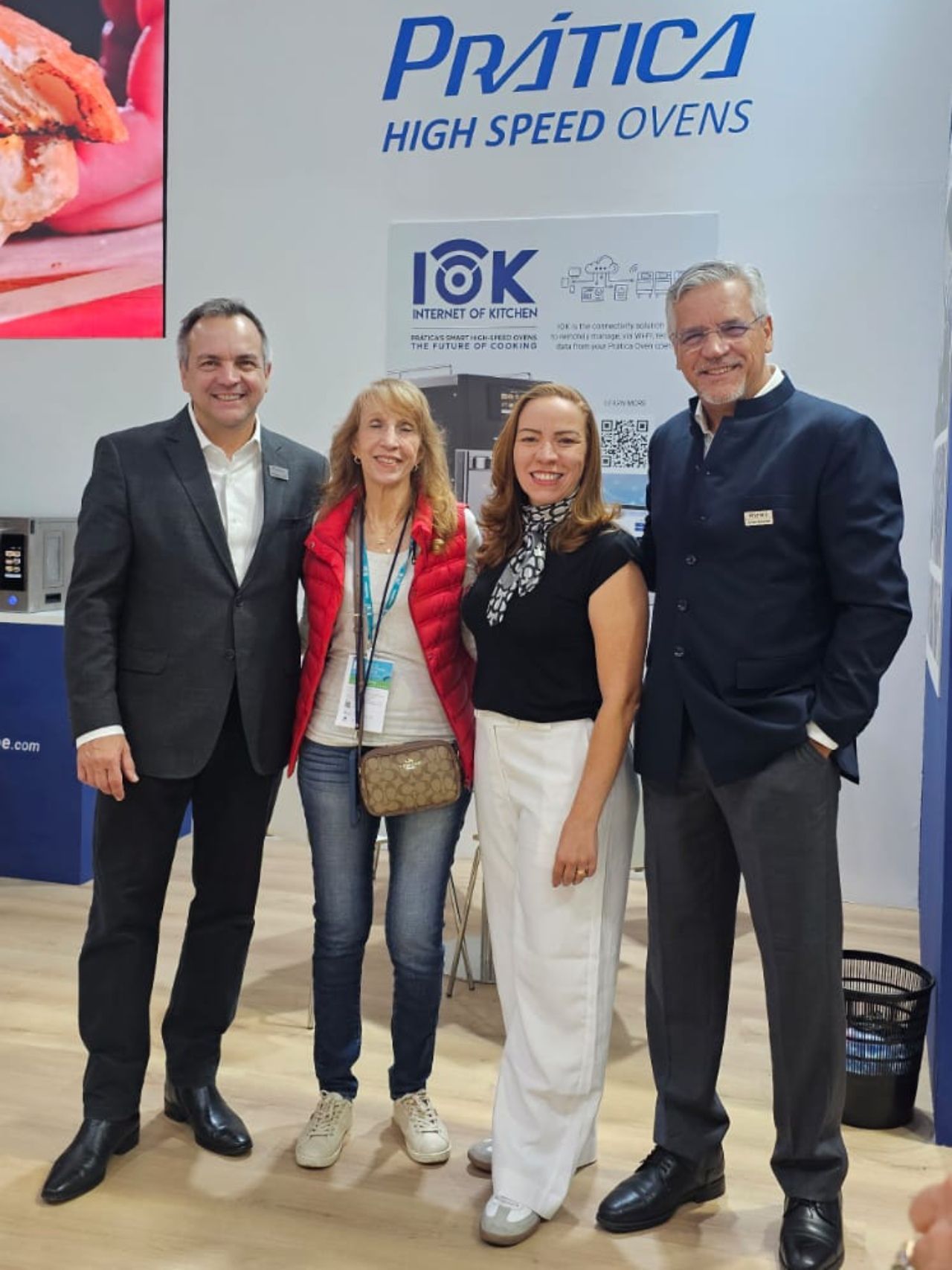 Four people pose in front of a Prática High Speed Ovens sign at a trade show.