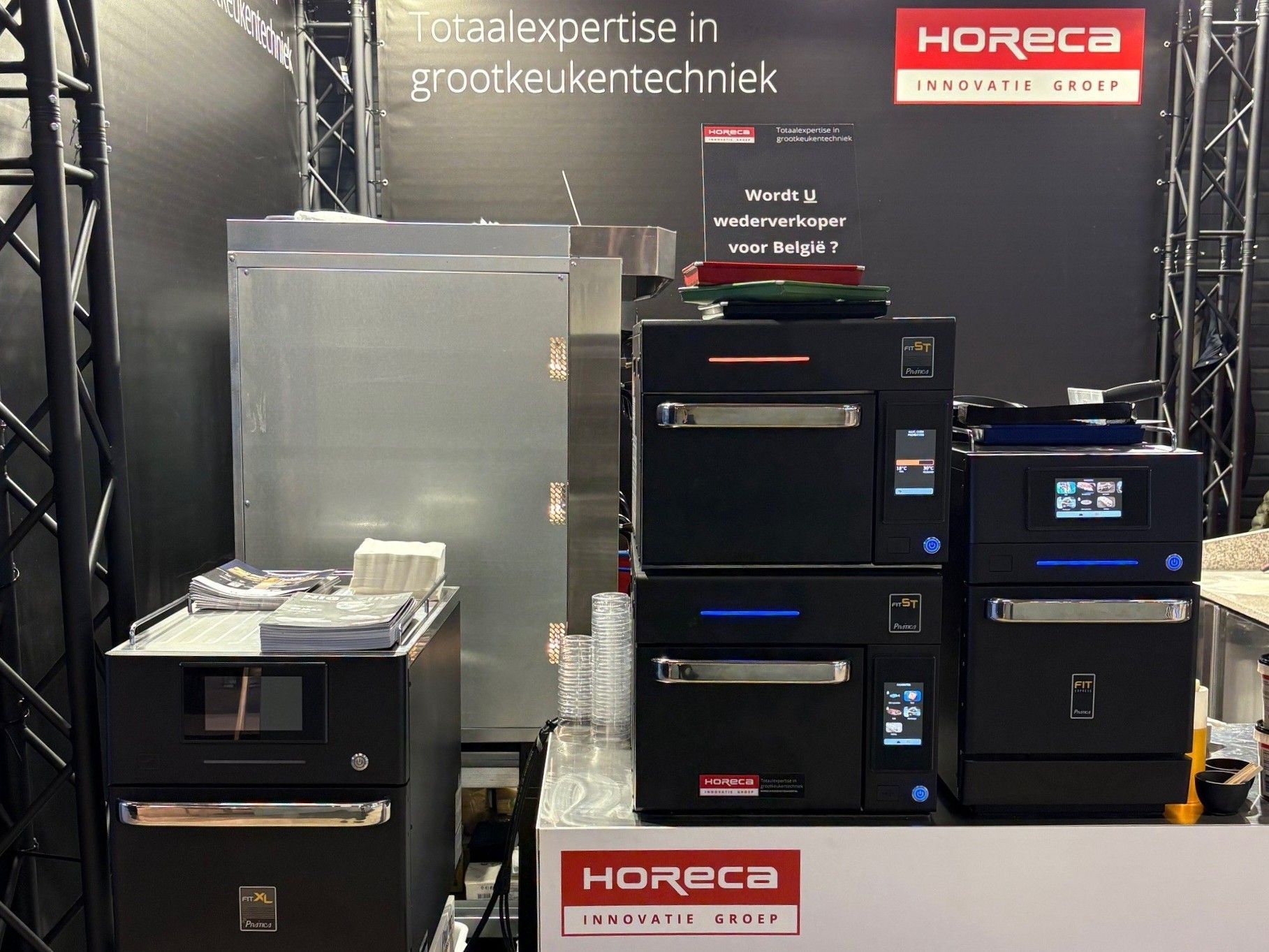 Display of commercial kitchen appliances at a trade show booth, featuring ovens and refrigeration units.