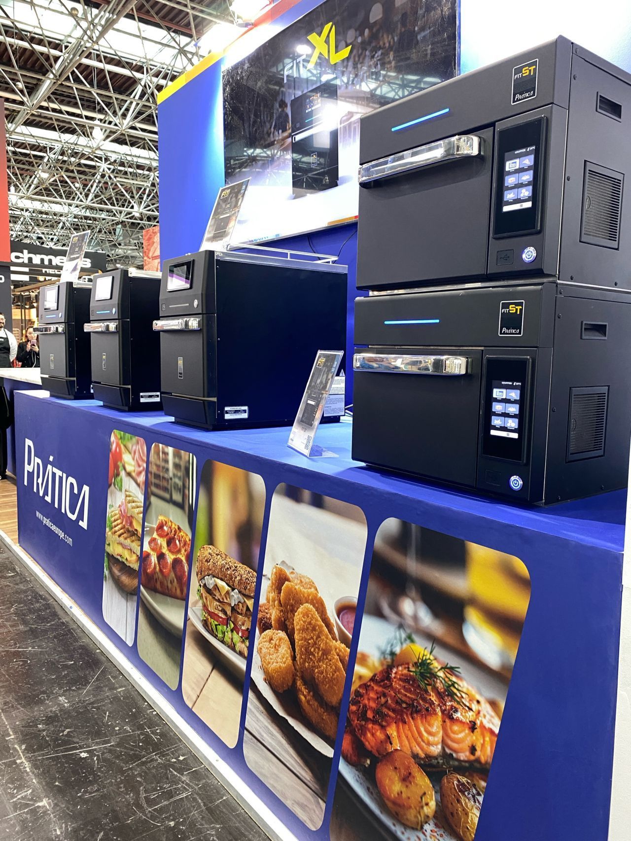 Display of black commercial ovens and food photos at a trade show booth.