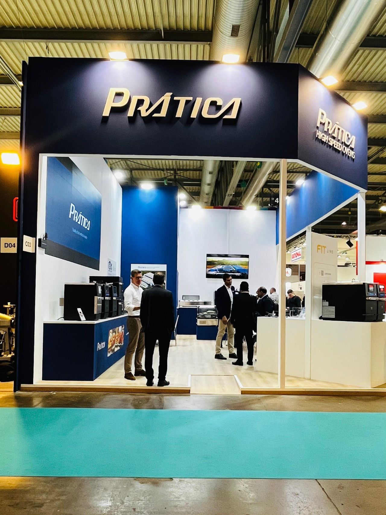 Pratica booth at a trade show; white and blue, people in suits inside.