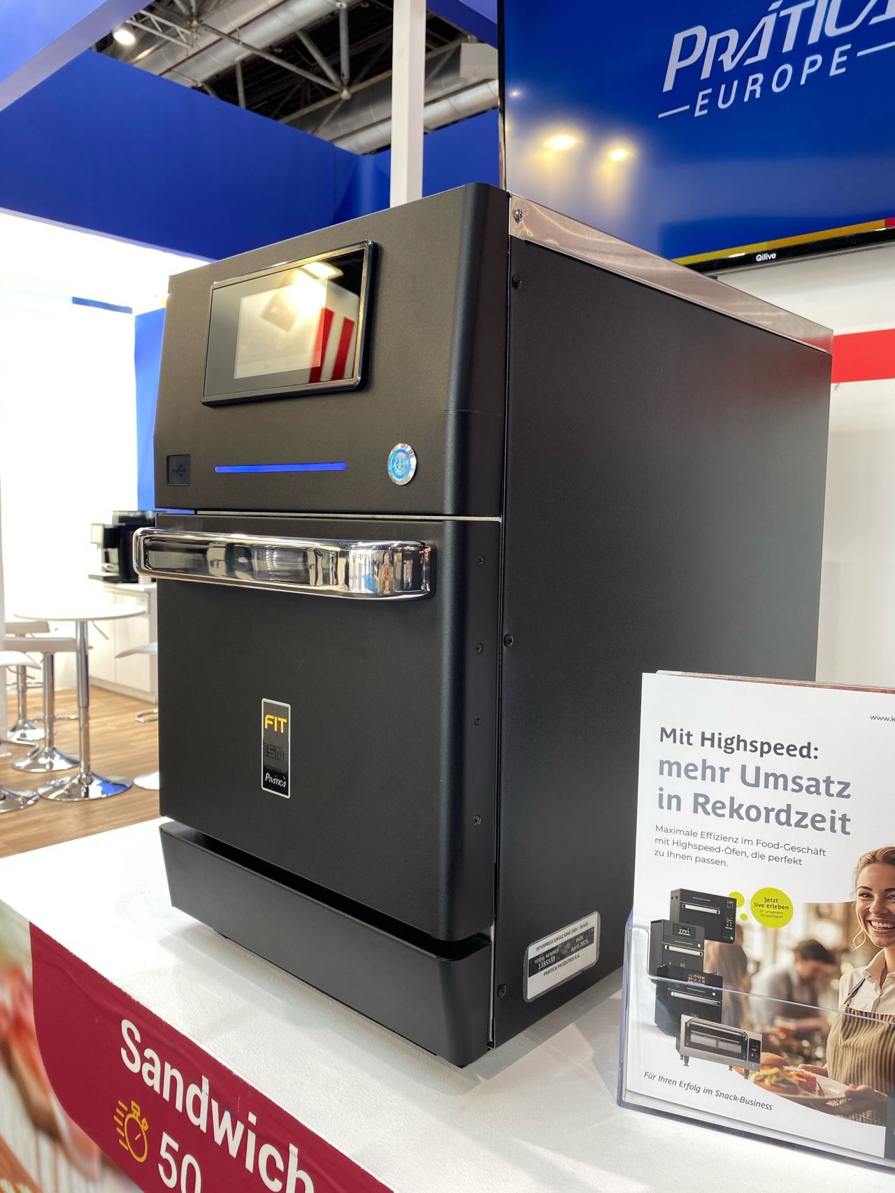 Black commercial oven with touch screen display, on a countertop at a trade show, advertisement.