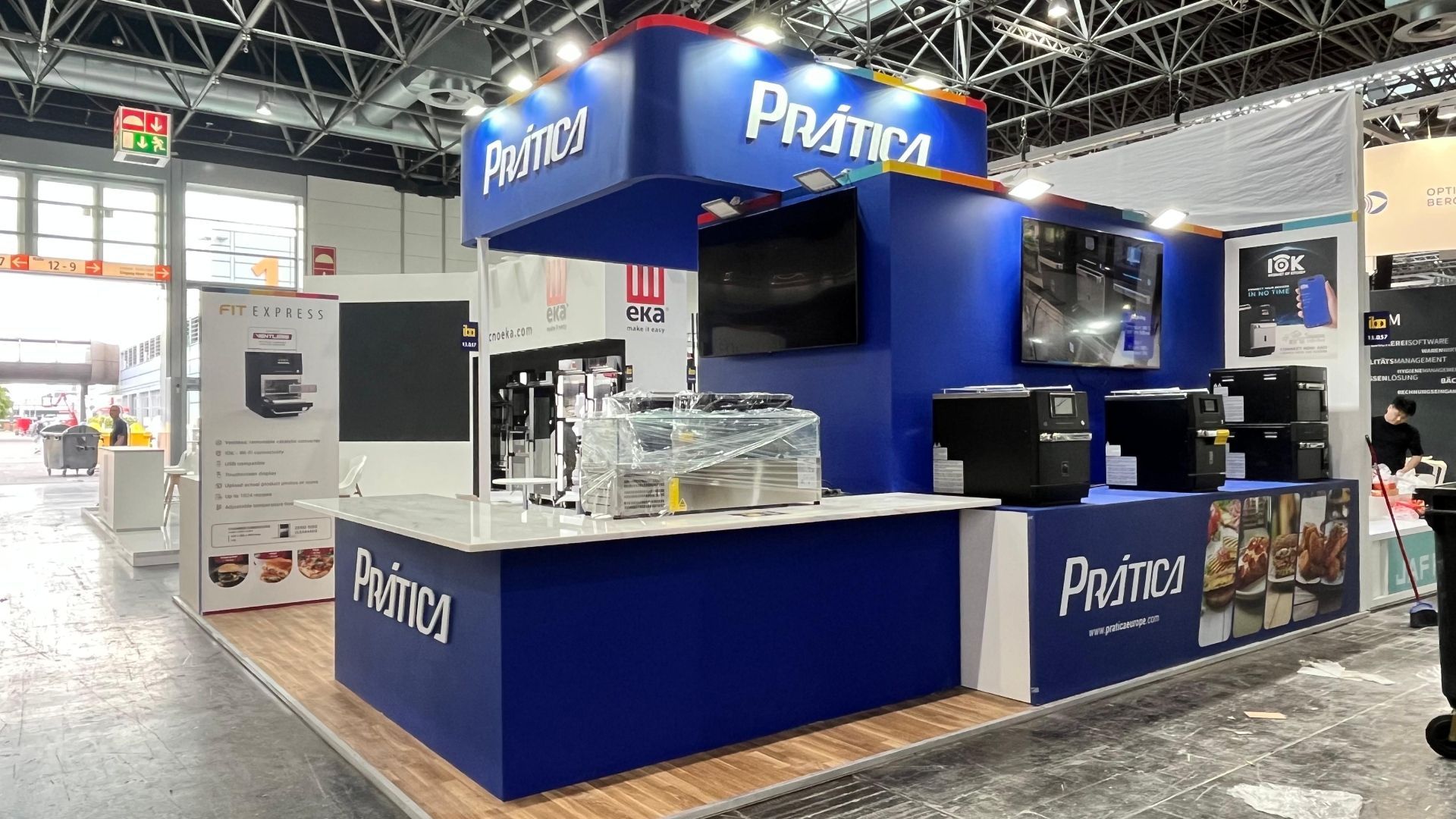 Pratica booth at a trade show: blue and white, showcasing appliances with displays and signage.