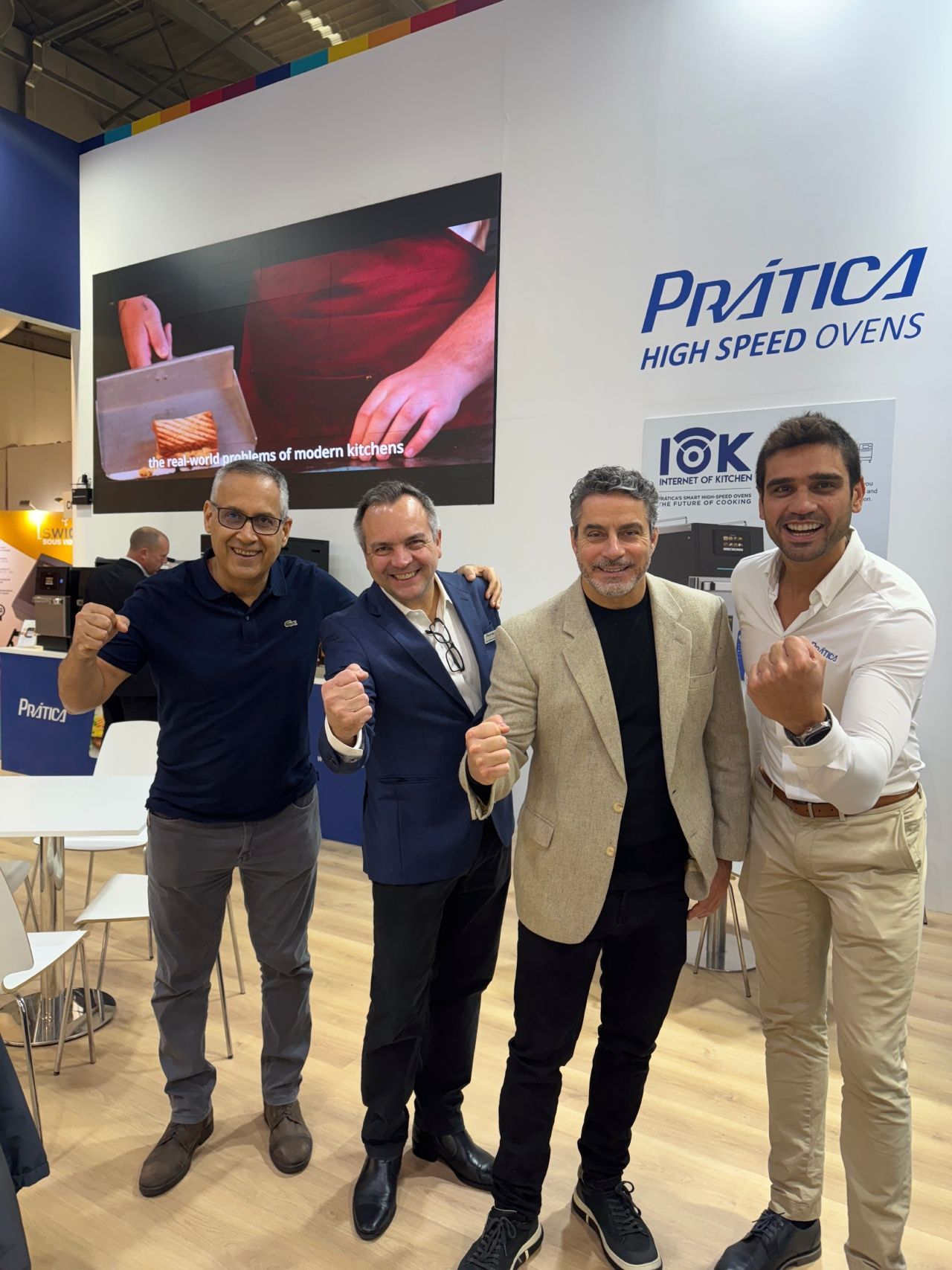 Four men smiling and flexing their arms in front of a booth for 