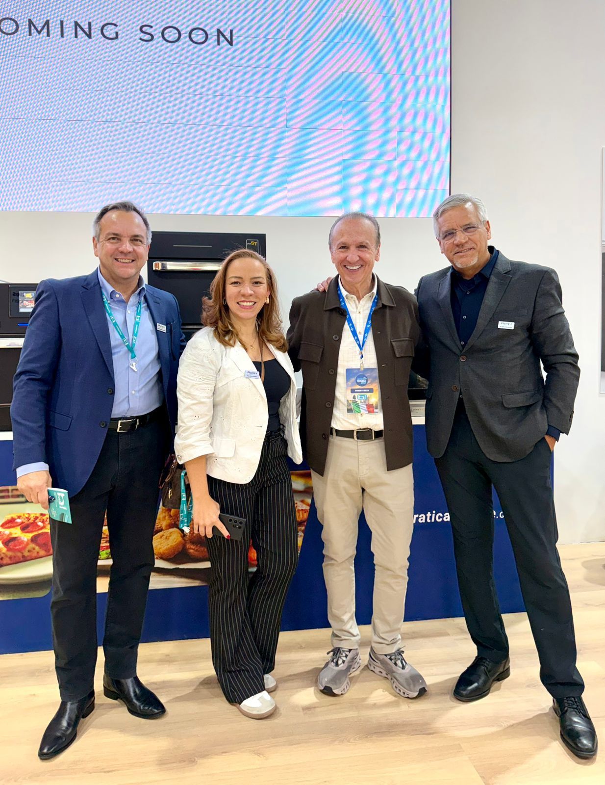 Four people posing for photo at a trade show booth; backdrop says 