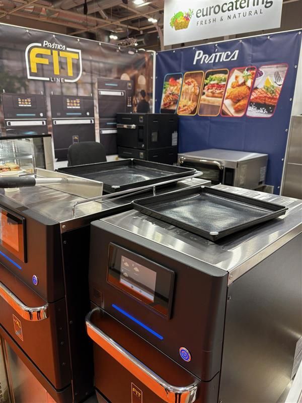A trade show booth featuring Pratica FIT commercial ovens with cooking griddles and a Eurocatering banner.