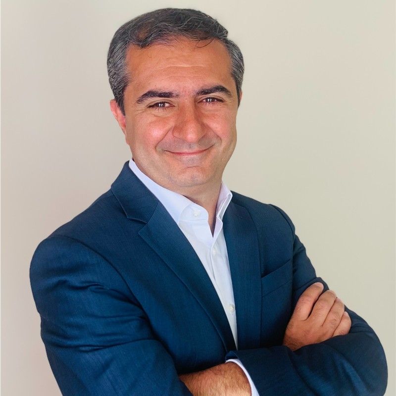 A man in a blue suit is smiling with his arms crossed