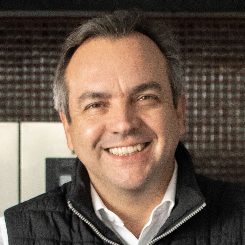 A man wearing a black vest and a white shirt is smiling for the camera.