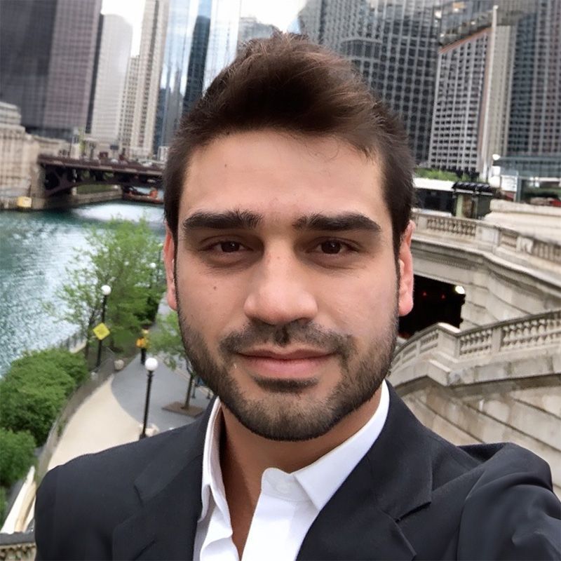 A man with a beard is taking a selfie in front of a bridge