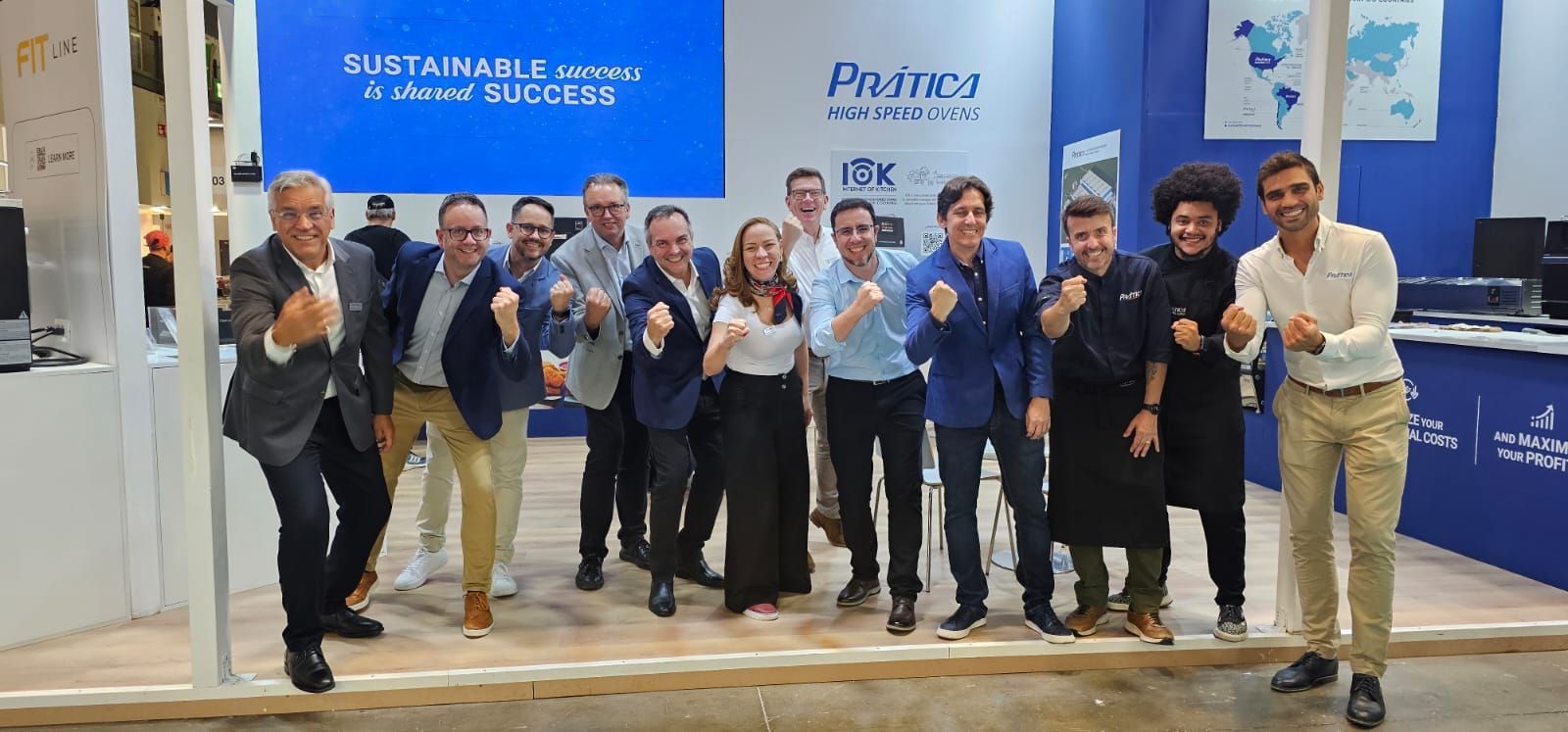 Group of people celebrating at a trade show booth, some with fists raised. Blue backdrop, booth branding visible.