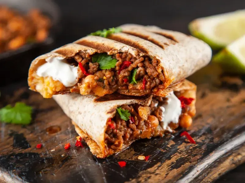 A burrito is cut in half on a wooden cutting board.