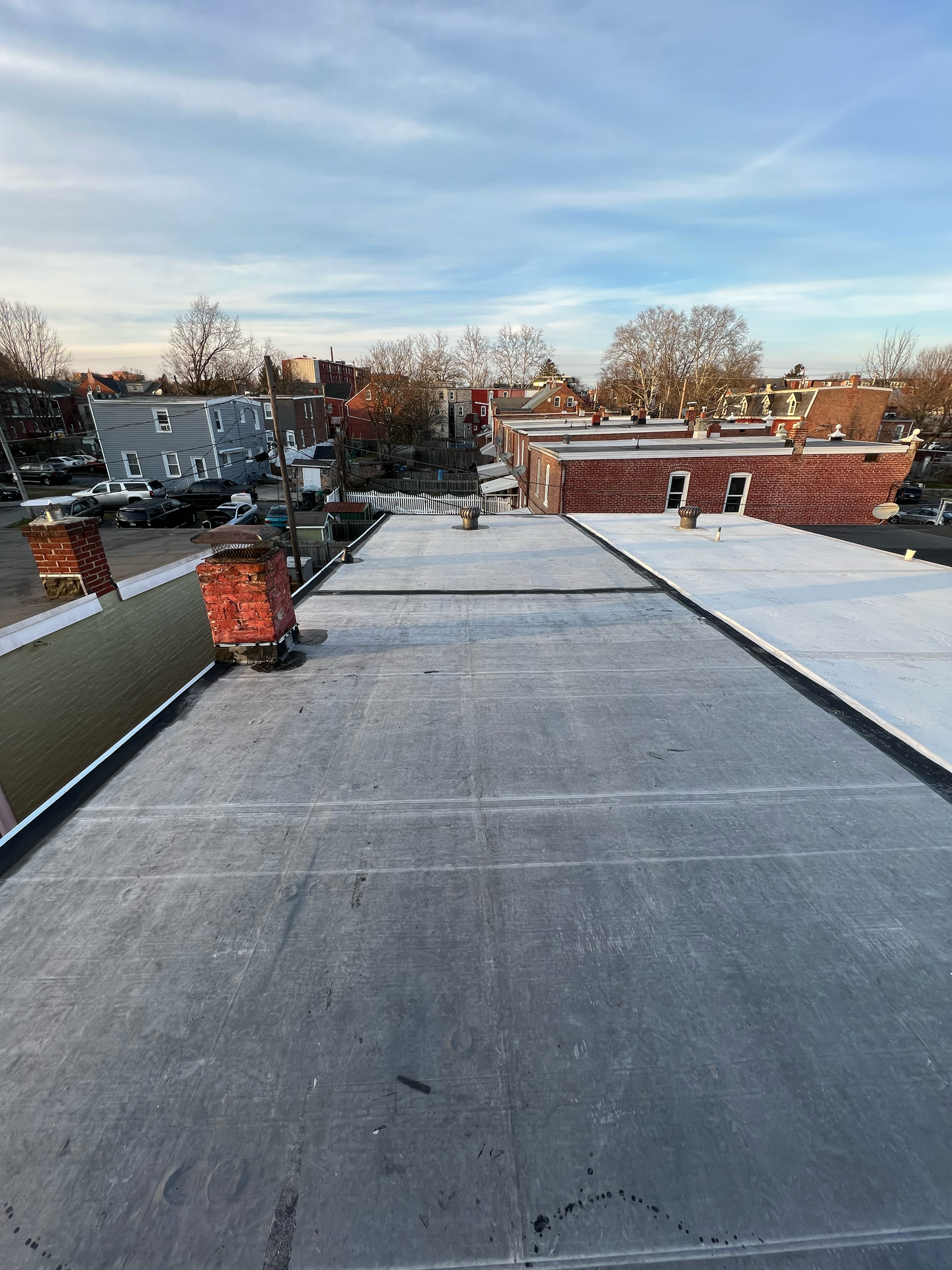 View from a rooftop with brick chimneys, black flat roof, and townhouses under a cloudy sky.
