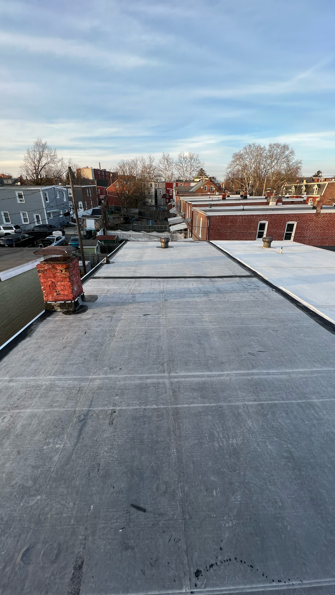Rooftop view of gray tar surface and brick buildings under a blue sky.