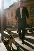 Person walking a dog on a leash outside a building in bright sunlight